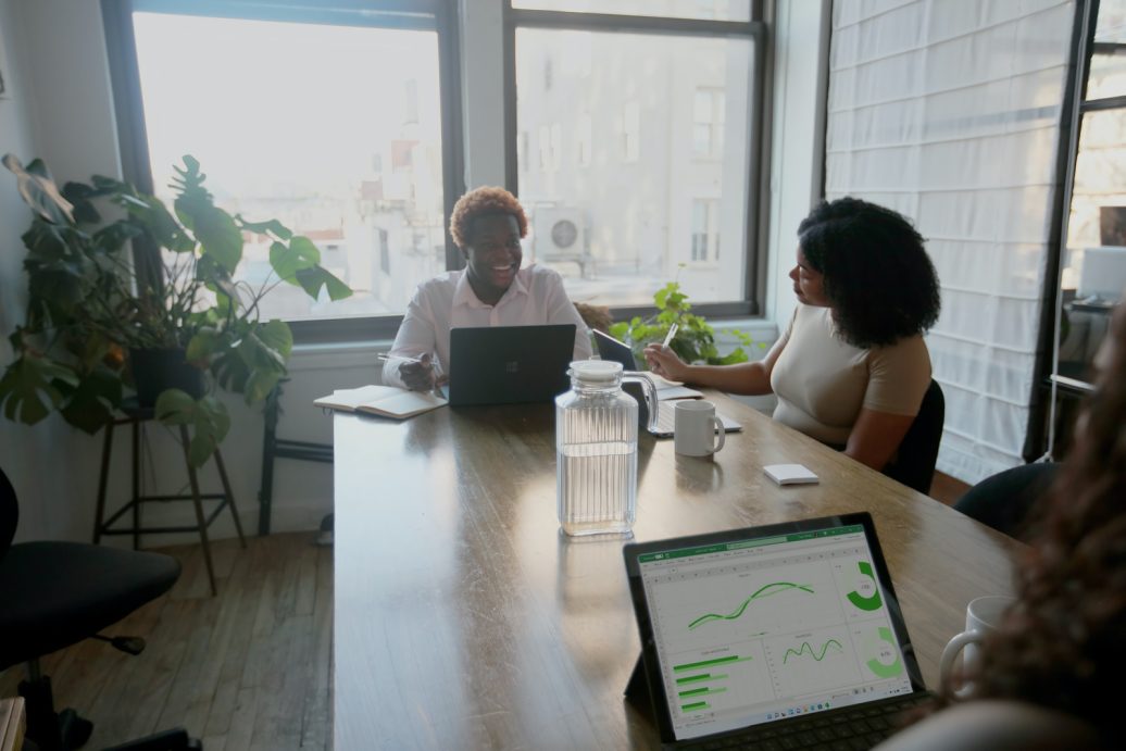 Three people at a table meeting at work with their Microsoft laptop